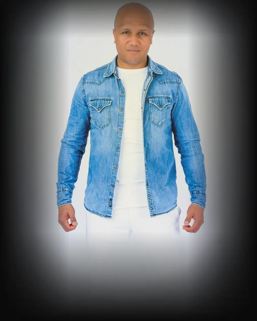 Michael Daimon, founder of Kizz Ryders, in a denim shirt lit against a dark ground